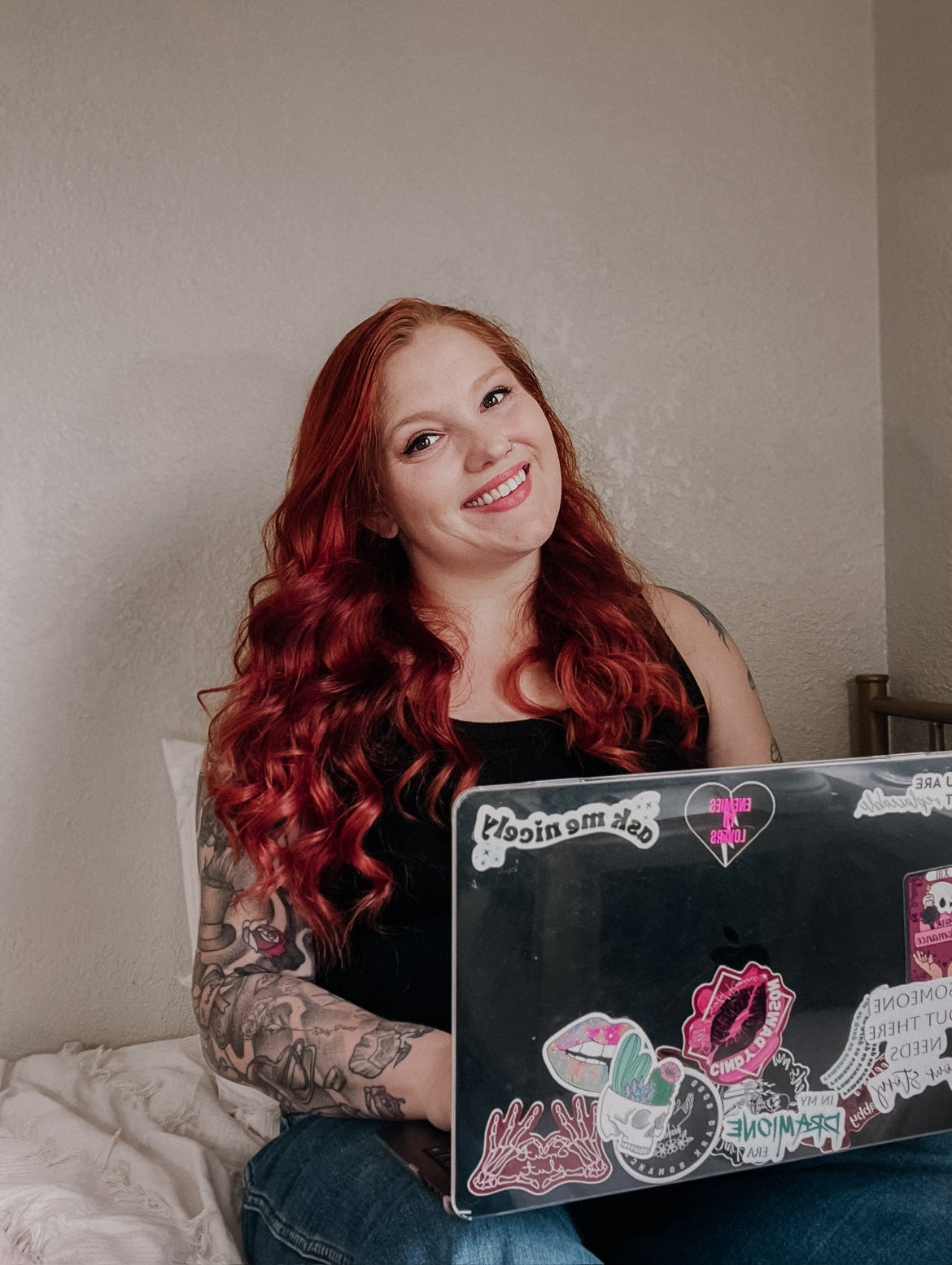 Author sitting on bed with computer, longer red hair and smiling